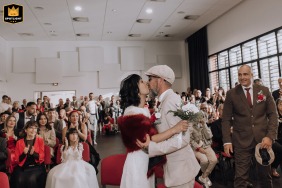 Bride and groom share a kiss after their civil wedding ceremony at Mondonville town hall, surrounded by guests and mayor.
